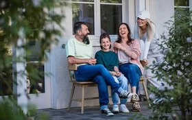 Eine Familie sitzt vor dem Haus auf einer Bank und lacht.